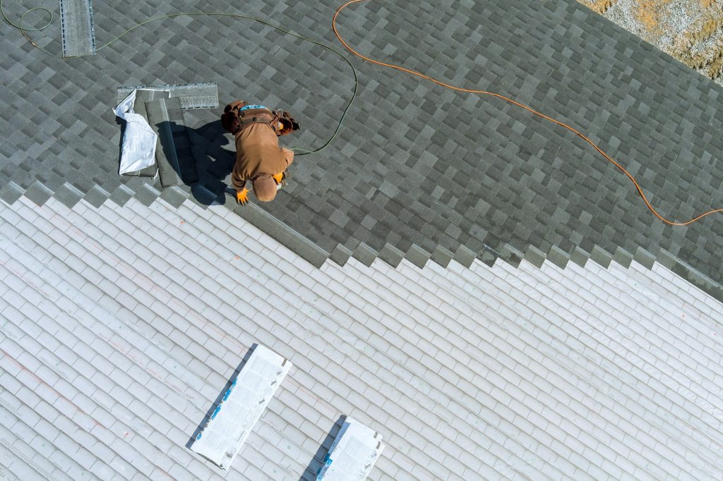 A worker installing shingles on the roof of a home